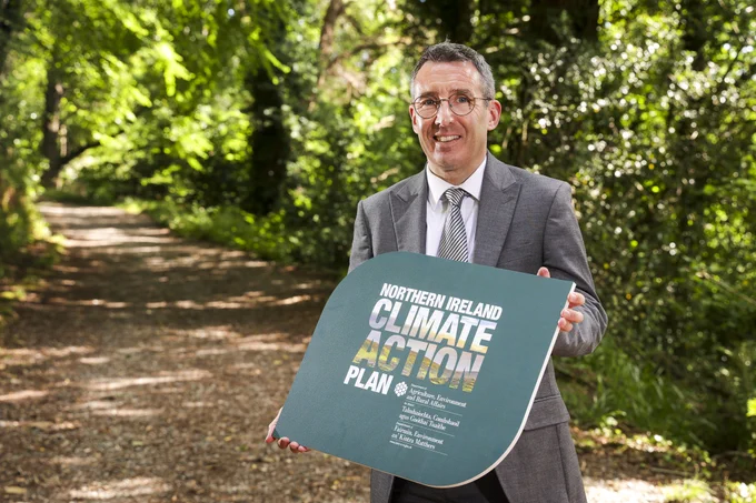 DAERA Minister Andrew Muir pictured holding Northern Ireland Climate Action Plan sign.