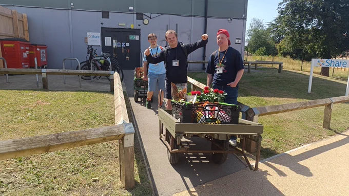 Three Share students using carts to transport plants. One of the students has his hands up in the air in celebration.