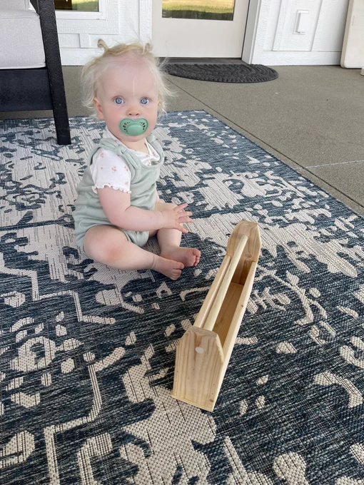 Small child sitting on the ground with a tiny handmade wooden toolbox in front of her.