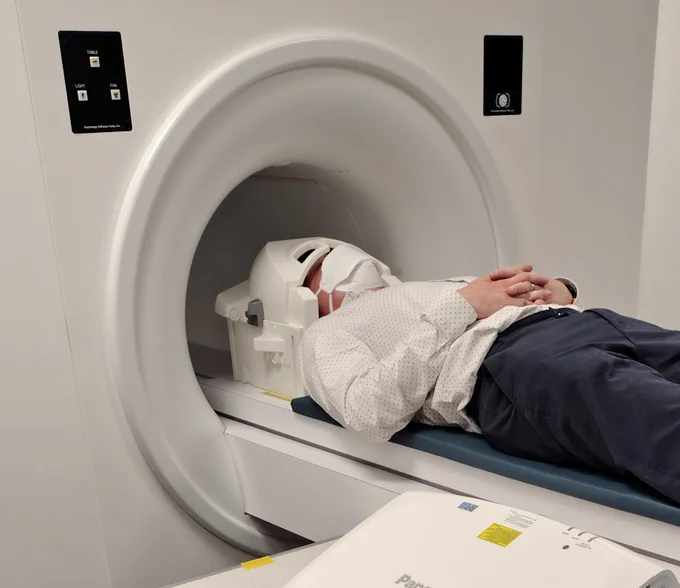 Man wearing a respirator mask lying in a "practise MRI scanner"