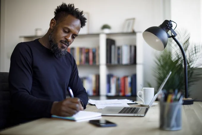 A guy writing notes on his desk alone.
