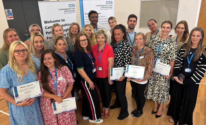 Group of NHS staff holding certificates, standing in a conference room with a "Welcome to Cambridgeshire and Peterborough NHS Foundation Trust" banner in the background.