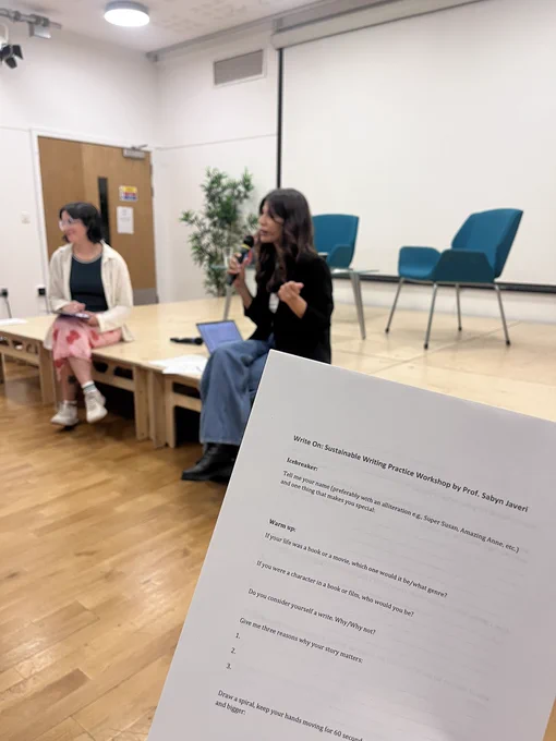 Yeisil and Sabyn perched on the stage. A white worksheet is held up, with the title ‘Write On: Sustainable Writing Practice Workshop by Prof. Sabyn Javeri.’