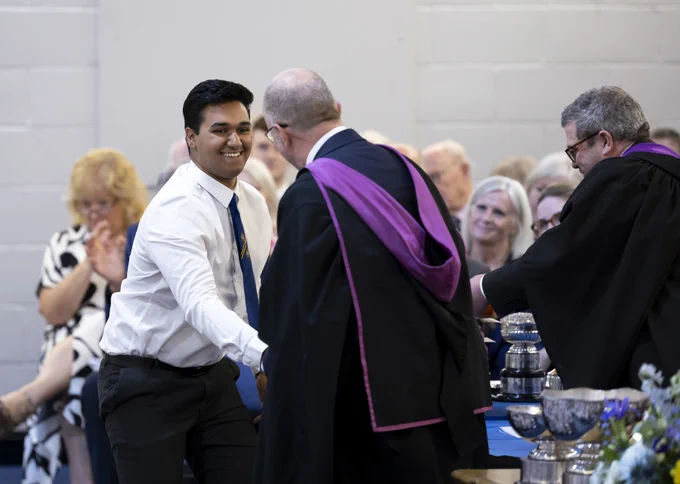 A Senior School pupil shaking the hand of the Rector, who is in a gown with purple highlights, at the Senior School Prizegiving Ceremony.