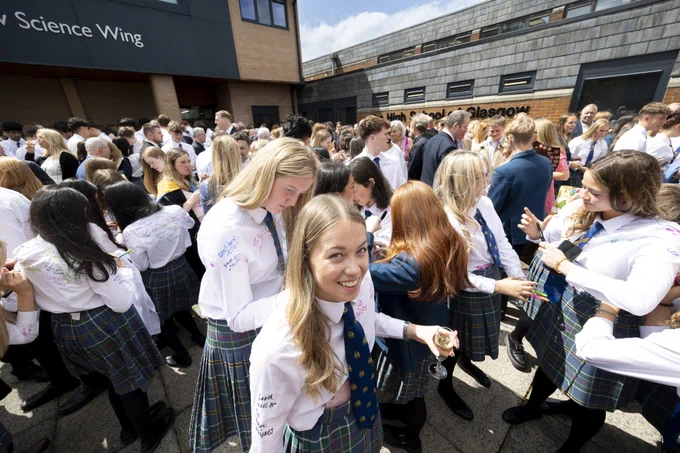 Senior School pupils gathered in the School courtyard. One girl is smiling at the camera as another signs her shirt, a tradition on the final day of school.