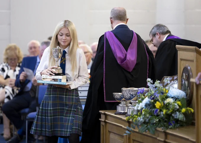 A Senior School pupil balancing a trophy on top of three books as she walks off stage at the Senior School Prizegiving Ceremony.