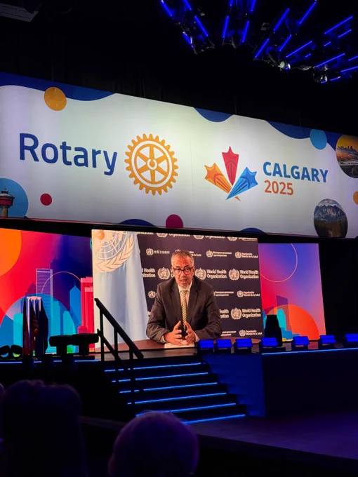 Person on stage at a Rotary International event, with a backdrop featuring the logo for "Calgary 2025" and various colorful designs.