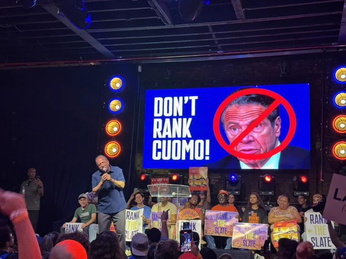 Photo of a rally showing Brad Lander speaking on stage in front of a screen that says don’t rank cuomo.