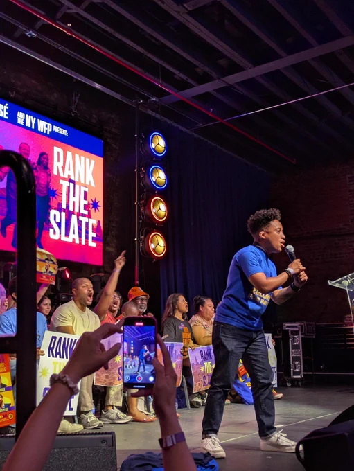 Photo of Crystal Hudson speaking at a rally in front of a screen that says: rank the slate.