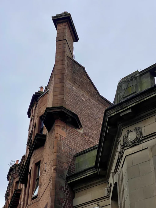 This is the canted chimney stack at the west corner of a rather good mixed use Glasgow Baroque tenement of 1910-12 at 271-285 Dumbarton Road in Glasgow. With its ground floor shops and red sandstone upper storeys, the tenement is by accomplished architects Campbell Douglas and Alexander Nisbet Paterson. The equally strong blonde sandstone cornice below is that of the Partick Library. Note how the gable is constructed of brick.