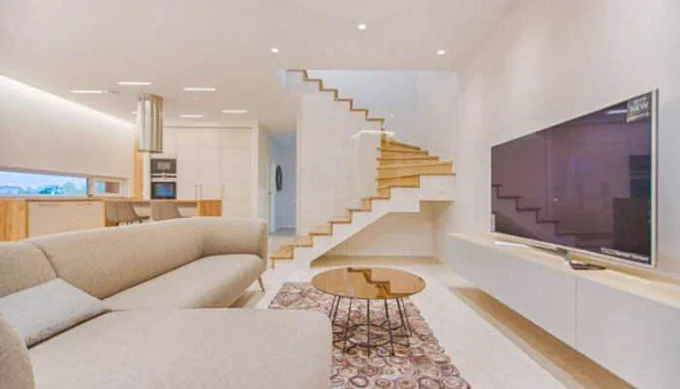 Modern living room with open kitchen and minimalist staircase, showcasing innovate home design with sleek furniture, soft lighting, and smart space utilization.