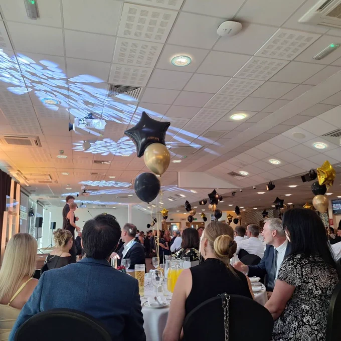Picture of the crowd sitting at tables during the awards ceremony. It's taken from the side of the room, and it also features the speakers standing on the stage.
