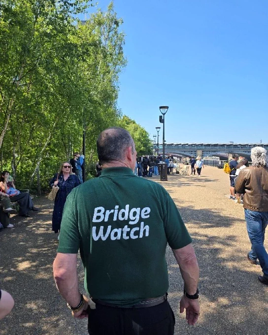 Gentleman outside in a public area, wearing a dark green t-shirt with 'Bridge Watch' written on the back.