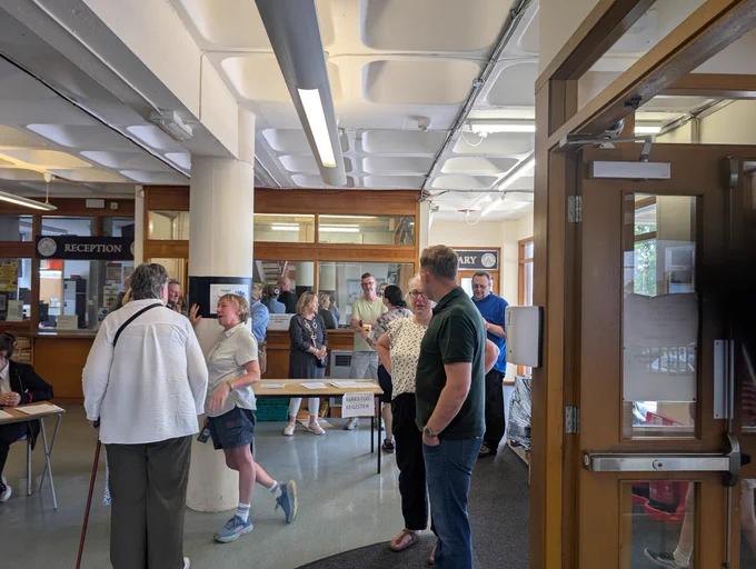 Various people scattered about the reception area of Craigie High School talking to each other. The entrance door can been seen on the right hand side, it is open.