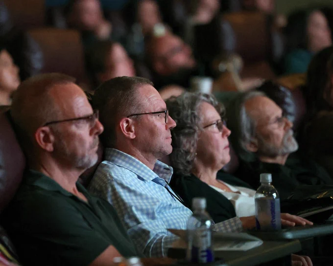 Side view of a large group of people watching a film on screen.