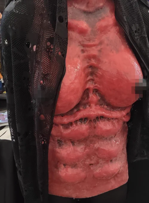 Wearable monster chest made of silicone and painted red with black nipples.  The rib cage is slightly jutting, the tits have a natural sag, the abdomen and collarbone is defined, and there is striation between the pectoral area that would suggest sinewy muscle beneath the fatty breast tissue.