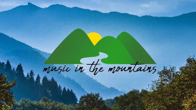 graphic of yellow sun behind green mountains with black text reading "music in the mountains" against a photo of blue sky and blue and green mountains