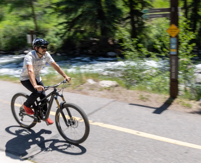Person riding a bicycle along a paved trail next to a flowing river, with motion blur indicating speed.
