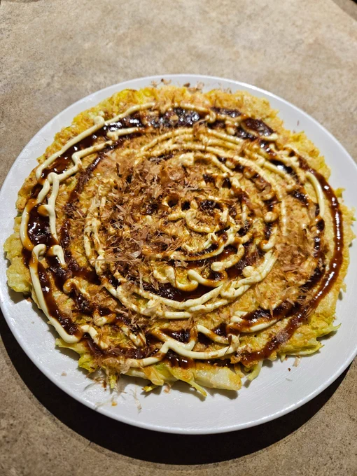 Dinner as described served on a round white plate. On the Okonomiyaki is drizzled the mayonnaise & Okonomiyaki sauce, and katsuobushi flakes on top of those.