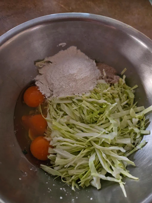 Okonomiyaki ingredients in a mixing bowl of thinly sliced cabbage, three eggs broken into it, a mix of flour & cornflour.