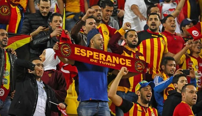 Imagem mostra torcedores com camisas amarela e vermelha do Espérance e uma faixa com o nome do time.