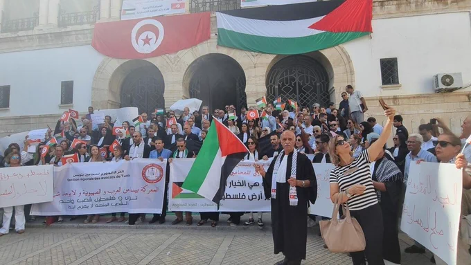 Imagem mostra um grupo de pessoas reunido à frente de bandeiras da Tunísia e da Palestina.