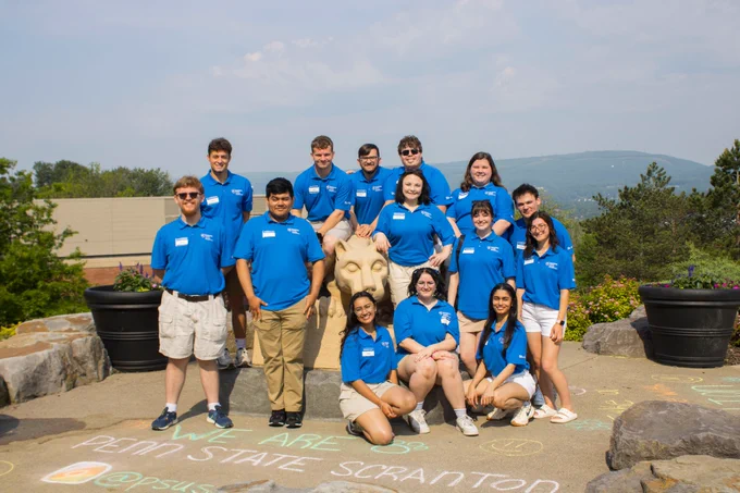 fifteen smiling students in penn state shirts pose near lion shrine statue  on penn state scranton campus