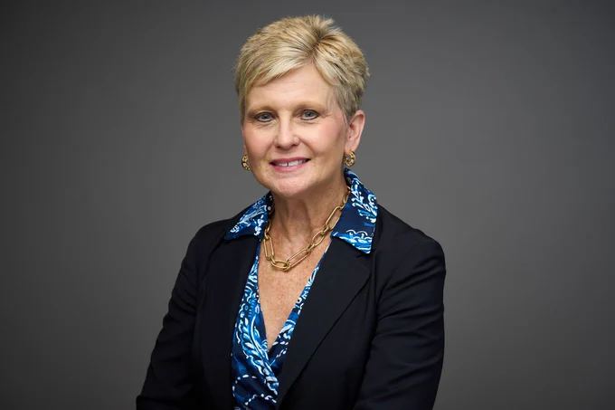 Portrait of Robyn Remotigue, smiling and dressed in a blue jacket with a patterned blue scarf and a necklace.