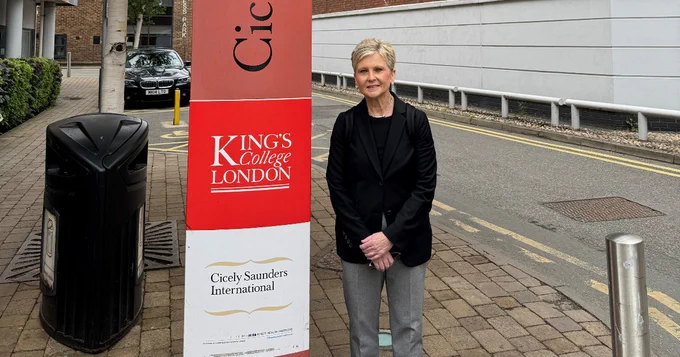 Robyn Remotigue standing next to a King's College London sign on an urban sidewalk.
