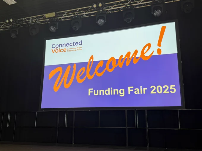 A picture of an orange, purple and white banner displaying the text ‘Welcome! Funding Fair 2025’, takent at Connected Voice’s annual Funding Fair at Northumbria University Students’ Union