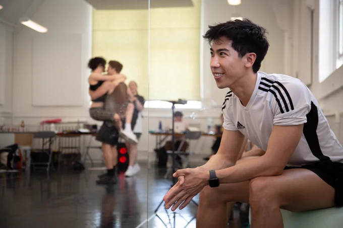 A photo showing a performer sat on a sofa while two people embrace in a reflection 