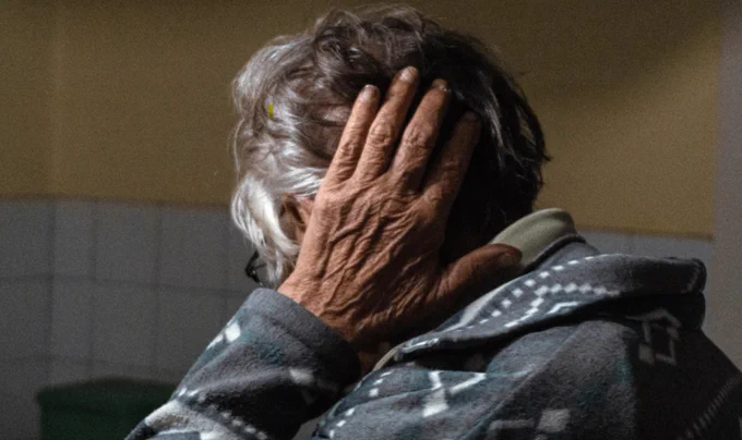 An image of a woman with grey hair holding the back of her head.