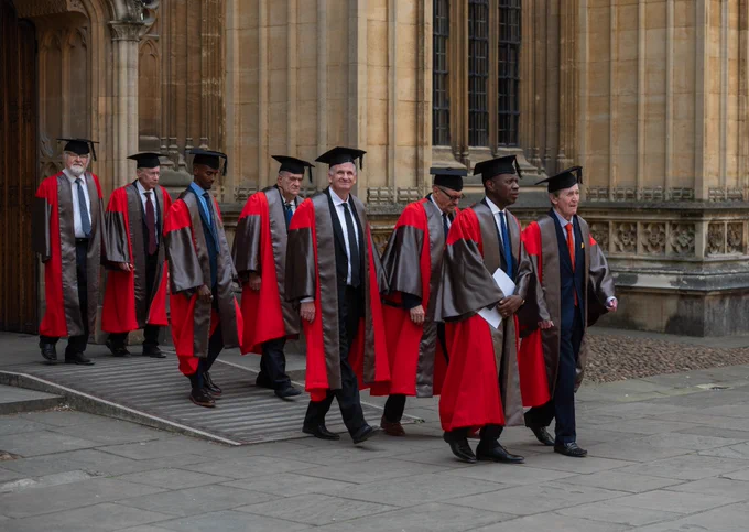 Eight Honorands in ceremonial robes walking together outside an Oxford University's Divinity School.