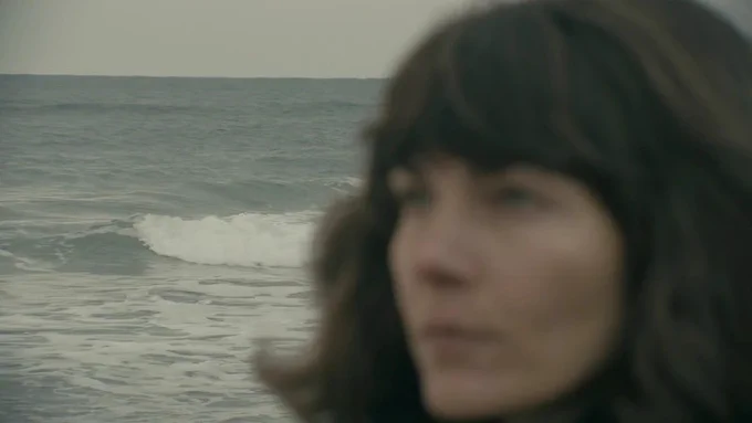 a blurry out of focus woman's face dominates the right hand half of the image - behind her, sharply in focus, are rolling waves