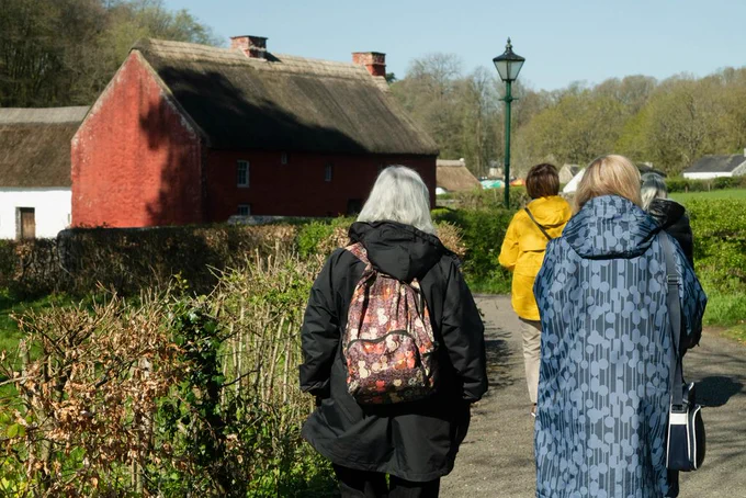 A group of people wearing coats walk towards a red building with their backs to the camera. 