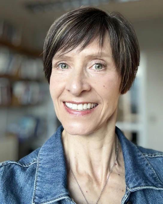 Close-up portrait of a smiling person with short hair, wearing a denim jacket.