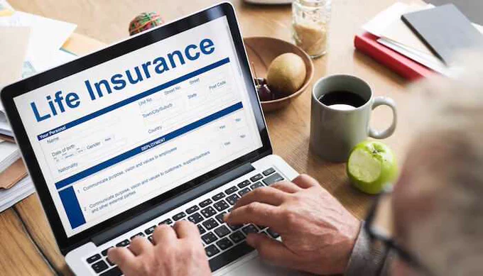 Person filling out a Life Insurance Policy form on a laptop at a desk with a cup of coffee and an apple nearby.