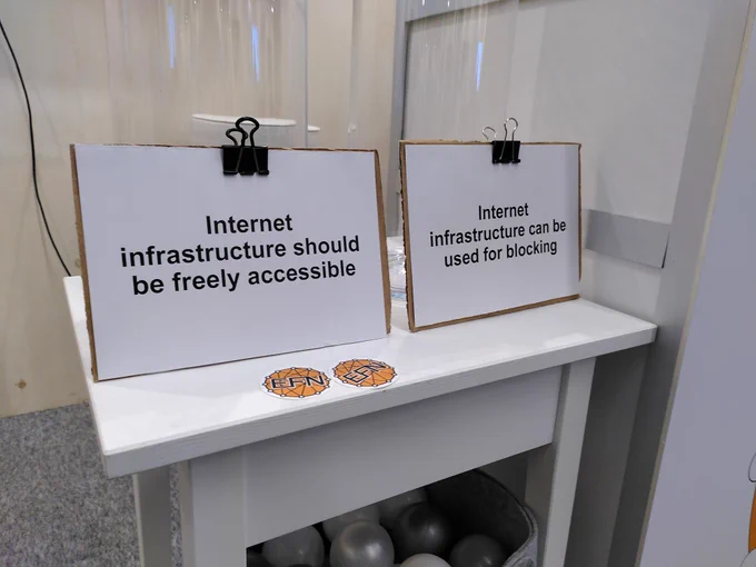 Two bowls representing two options of a vote, on a small table. Both are empty. The two options for voting are on pieces of paper in front. They say "Internet infrastructure should be freely accessible" and "Internet infrastructure can be used for blocking"