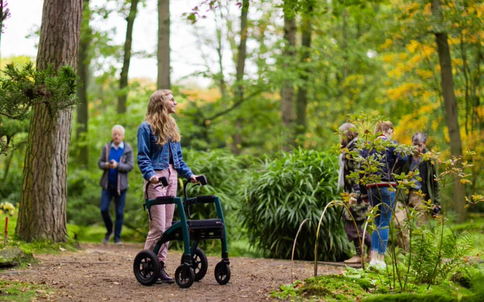 A young disabled person walking through a forest with a mobility aid.