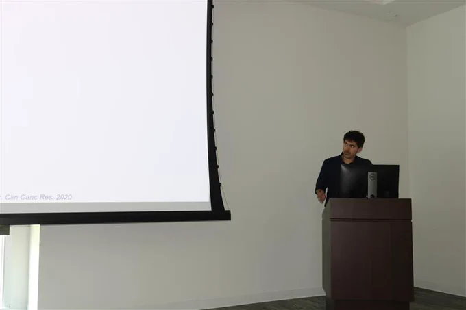 A man in a black suit standing behind a podium and presenting a powerpoint presentation.