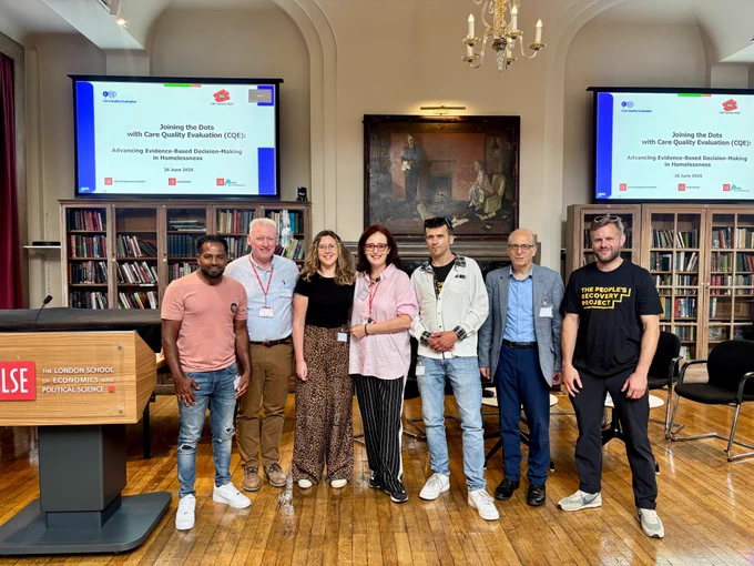 A photo taken before the event started with Dr Michela Tinelli, representatives from across the project, and event speakers for the all gathered in a line in front of a podium.