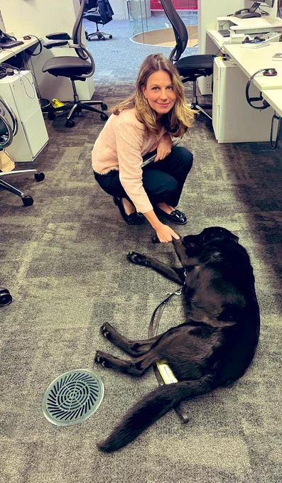 Shawn the guide dog lying on the floor resting with his paw in Helena’s hand.