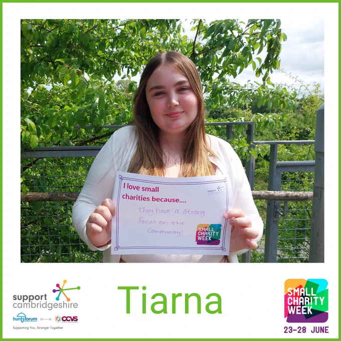 Photo of Tiana. She has long blonde hair; she is wearing a white top and is standing outside by a bush smiling.  

She holds a piece of paper that reads “I love small charities because they have a strong focus on the community” 

We also see her name, ‘Tiarna’ and the Small Charity Week and Support Cambridgeshire Interim logos. 