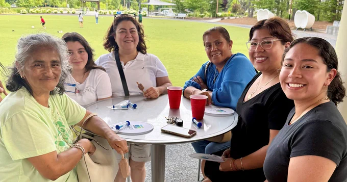 Family smiling while sitting around a table in an outdoor setting 