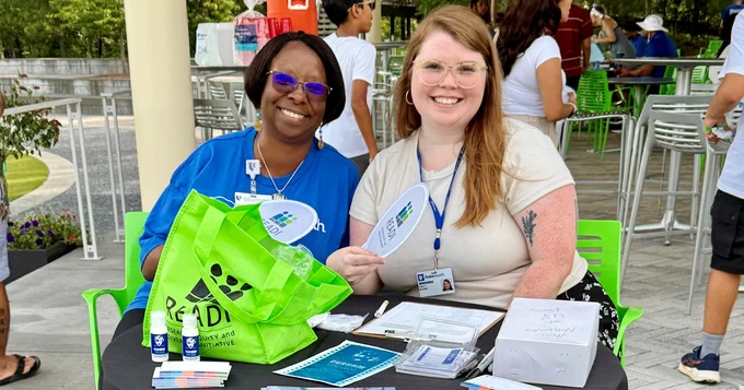 Two people sit at a greeting table smiling with materials around them