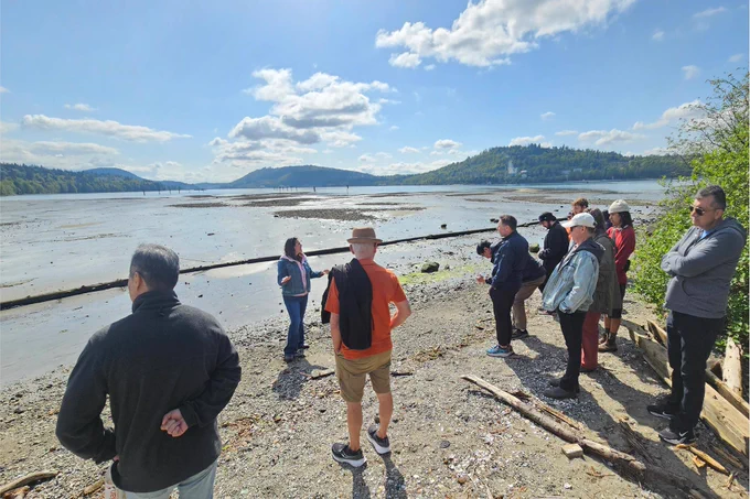 People standing on a beach facing a person, who has the water and distant mountains behind them.