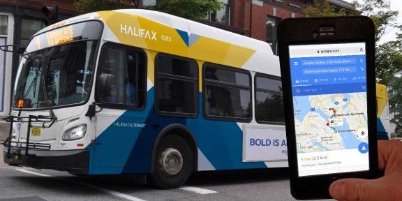 A bus is stopped at a crosswalk. Someone is holding a phone with Google Maps open in front of the bus.