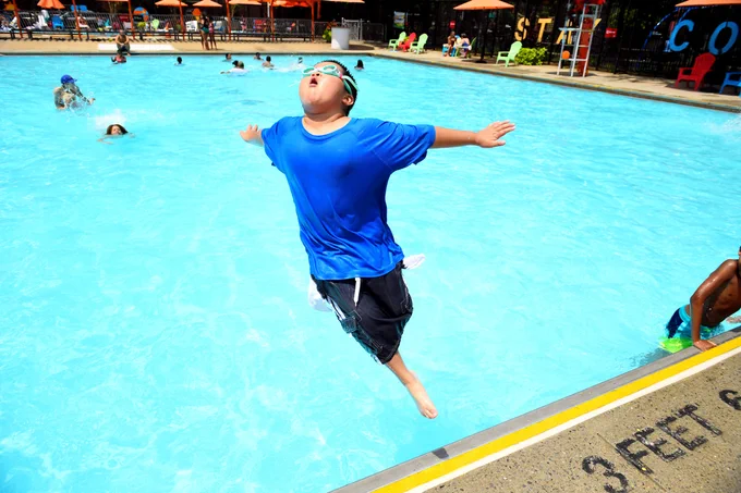 A young swimmer happily jumps into the pool. His head is titled up to the skies, his arms are splayed out, and summer is officially here!