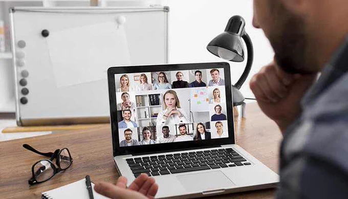 A person participating in a virtual meeting using popular Video Chat Sites, with multiple colleagues displayed on the laptop screen during a video conference.