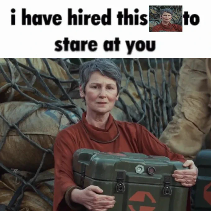 An edited image: a white header above a screenshot. The header reads, in slightly low quality black text, "i have hired this ___ to stare at you." In the space is a stretched version of the image below: a screenshot of the Force Healer from Andor, a woman with white skin, a long face, and rosy cheeks: her dark grey hair is trimmed into a short pixie cut, and she's wearing a robe-like rust-coloured top, and holding a green crate in her arms as she performs work on Yavin. She's staring directly into the camera with a ponderous look on her face--or, in the episode, directly at Cassian offscreen, as he's walking to the U-wing to leave for Kafrene.
